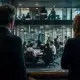 Two professionals observing a team meeting in a contemporary office space.